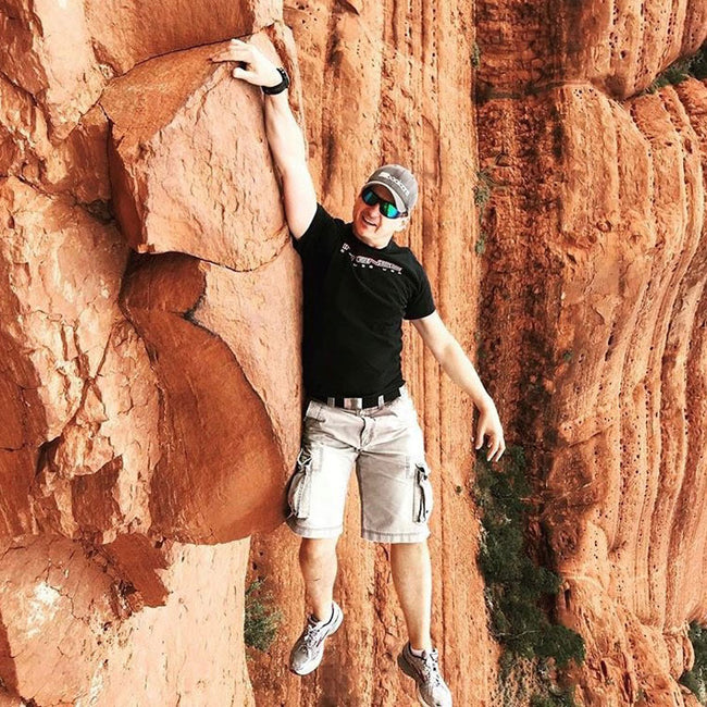 man climbing a rock wearing the booicore baseball cap grey