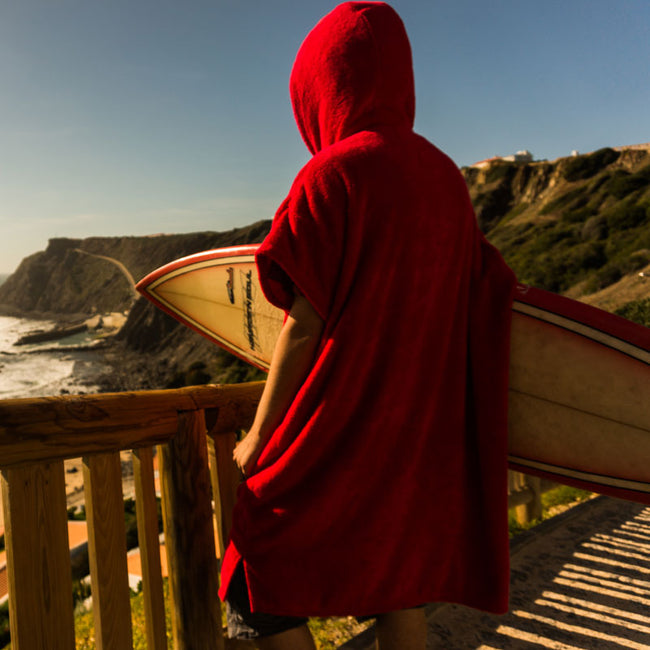 person wearing a booicore changing robe satanic red , holding a surfboard and looking out to sea