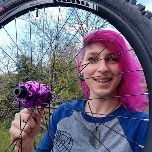 woman with pink hair wearing the booicore baseball tee - pictured through a mountain bike wheel