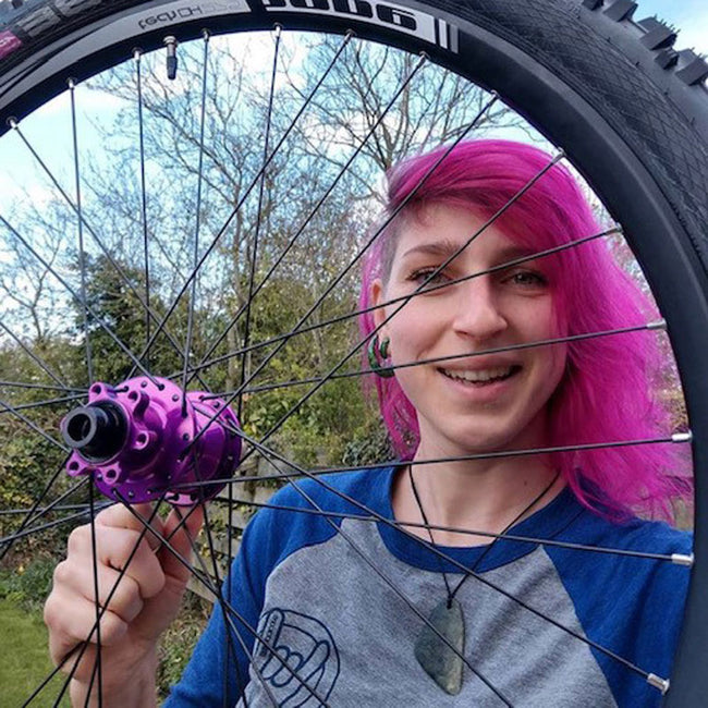 woman with pink hair wearing the booicore baseball tee - pictured through a mountain bike wheel